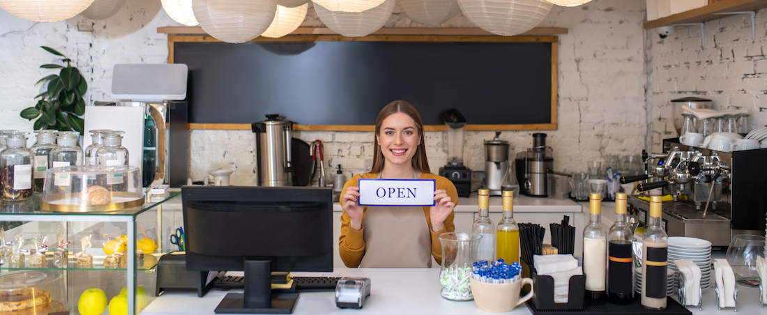 smiling cafe owner holding the open sign